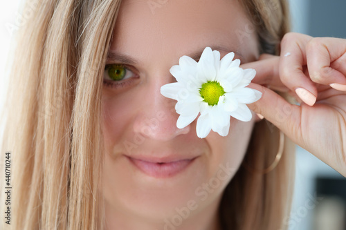 Portrait of beautiful young woman with green eyes closes one eye with flower