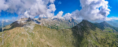 Vibrant aerial panoramic of the Alps during springtime. Snow capped peaks, forest covered valley and glacier fed streams and waterfalls