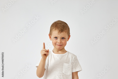 Portrait of a boy with a funny face and a white T shirt pointing up on a white background