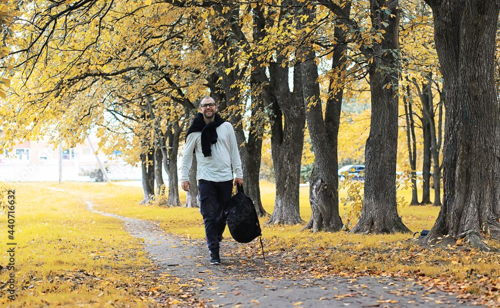 Fototapeta premium A young man in glasses walks in the park with an umbrella during the rain.
