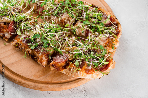 Pinsa romana with salami, cheese, mushrooms, decorated with microgreens on wooden boardon white background. photo