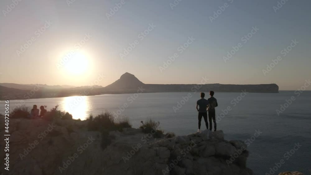 Two buddies watch sunset on top of cliff. Ocean view, Cape Prim, Javea. Aerial pullback Two buddies watch sunset on top of cliff. Ocean view, Cape Prim, Javea. Aerial pullback