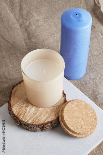 blue and beige aroma candle in a glass on a wooden podium from a saw cut from a tree. natural candles for aroma therapy
