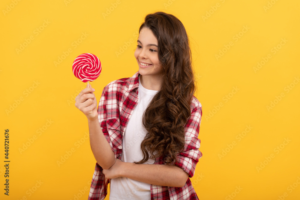 cheerful child with long curly hair hold lollipop caramel candy on yellow background, dental health. cheerful child with long curly hair hold lollipop caramel candy on yellow background, dental health.