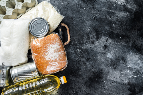 Kitchen table with Donation food goods, quarantine help concept. Oil, canned food, pasta, bread, sugar, egg. Black background. Top view. Copy space