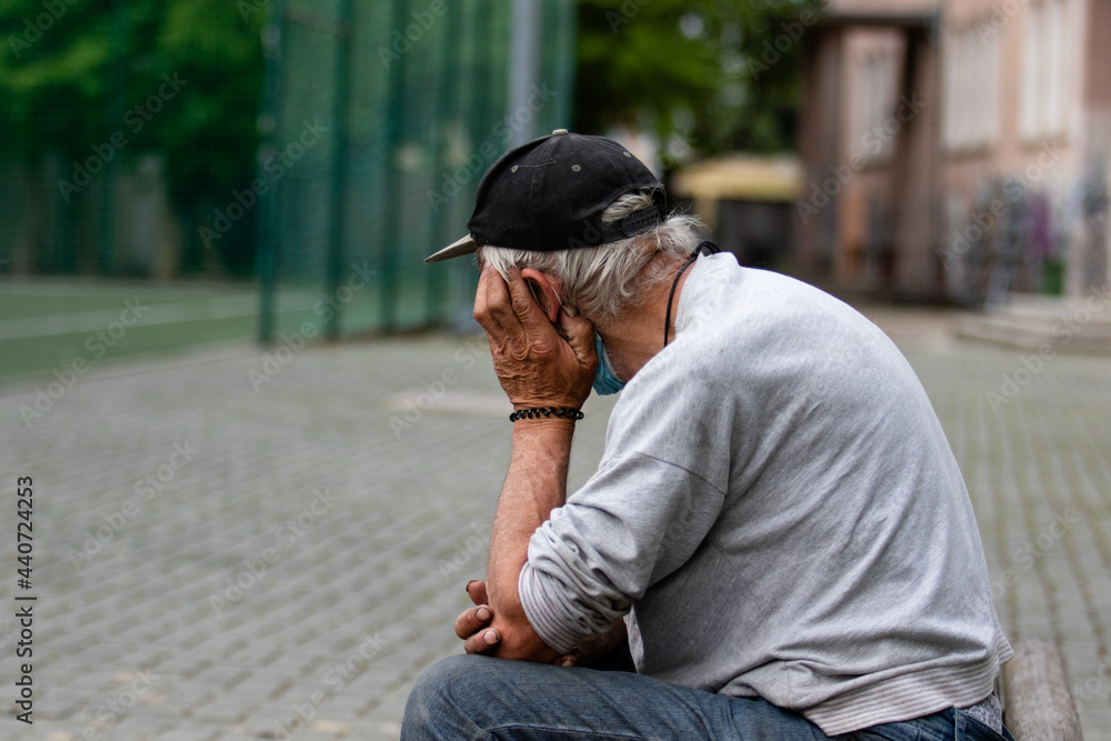 An elderly gray-haired man in a black cap sits sadly on a bench An elderly gray-haired man in a black cap sits sadly on a bench