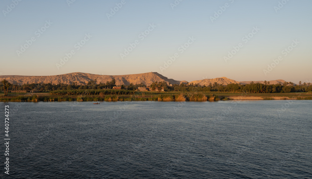 Panoramic sunset view of a rower on the Nile River near Luxor, Egypt with landscapes in the background