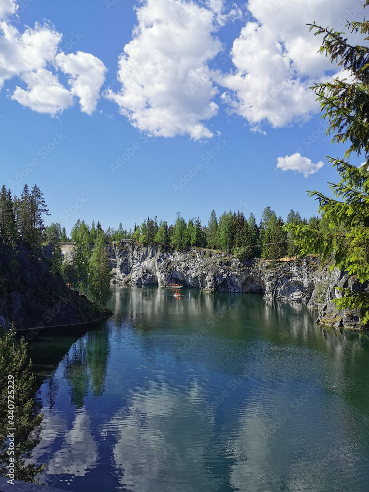 View from the observation deck of the emerald water of the Marble Canyon in the Ruskeala Mountain Park with the reflection of the sky and clouds on a sunny summer day. View from the observation deck of the emerald water of the Marble Canyon in the Ruskeala Mountain Park with the reflection of the sky and clouds on a sunny summer day.