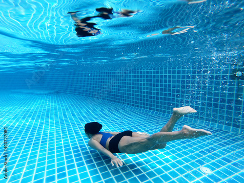 Woman swimming underwater or diving in the swimming pool, as background. Summer or sports concept.