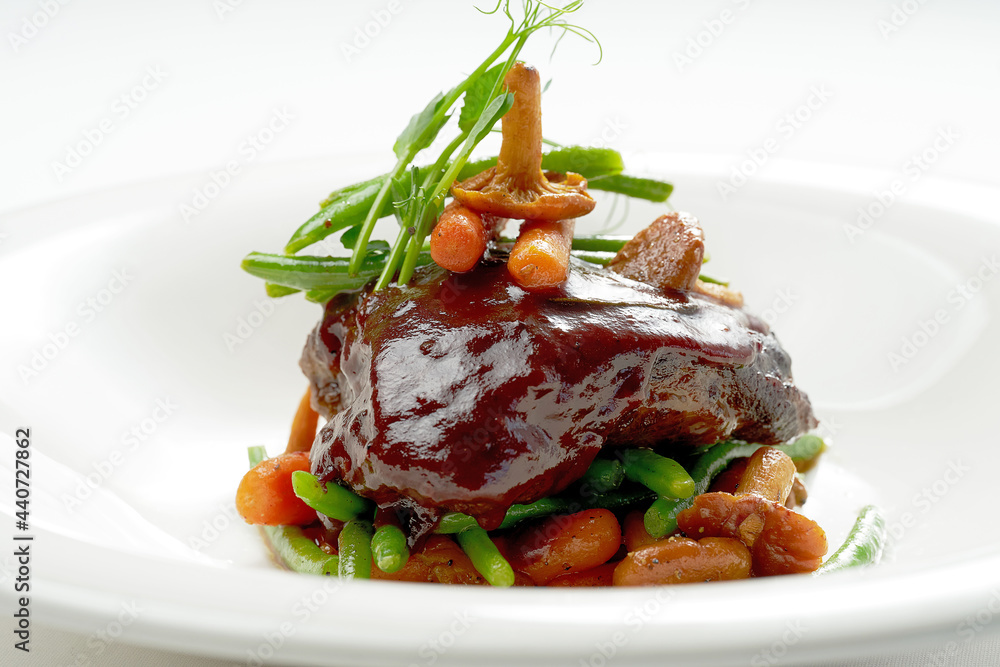 Beef cheek steak, caramelized in wine sauce with chanterelles and asparagus in a white plate. Isolated on grey background. Beef cheek steak, caramelized in wine sauce with chanterelles and asparagus in a white plate. Isolated on grey background.