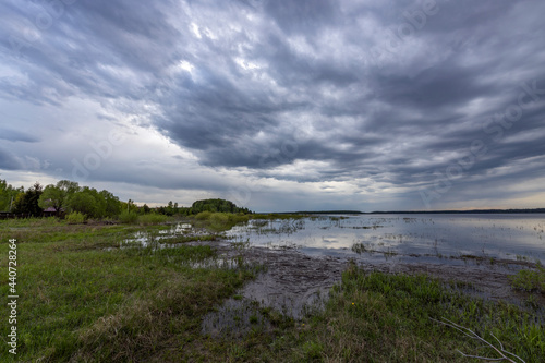 Evening landscape, The dramatic sky is reflected in the water. Green spring grass in the foreground.