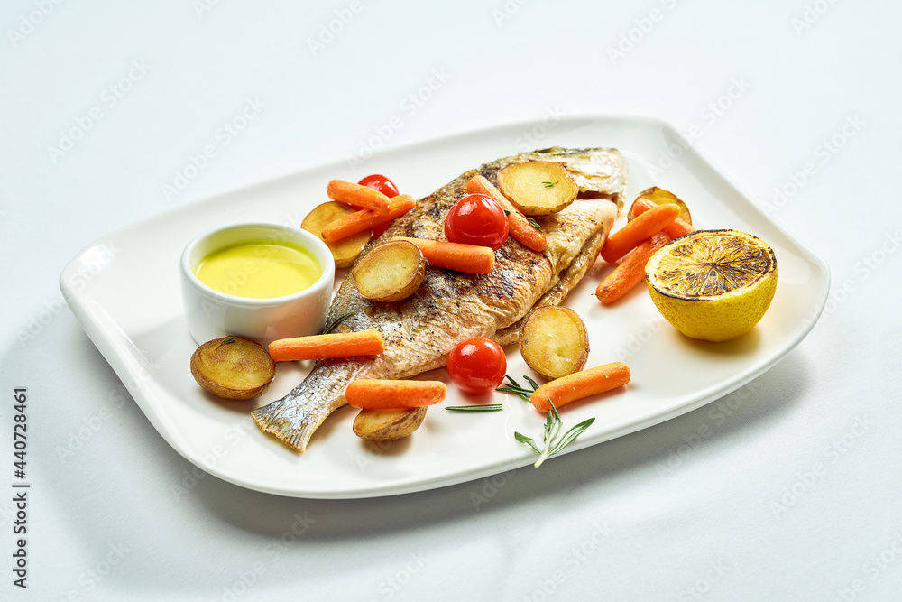Grilled dorado with potatoes, carrots, and cherry tomatoes in a white plate. Isolated on white background. View from above