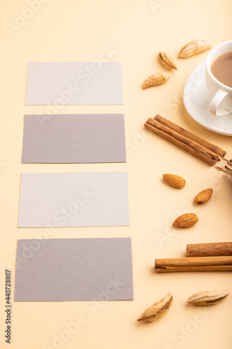 Composition of gray paper business cards, almonds, cinnamon and cup of coffee. mockup on orange background. side view, copy space.