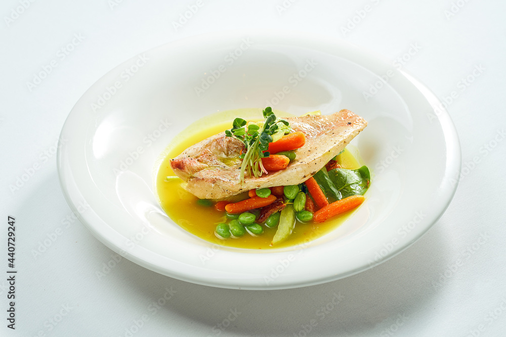Fried Sea bass fillet with stewed vegetables and orange sauce in a white plate. Isolated on grey background.