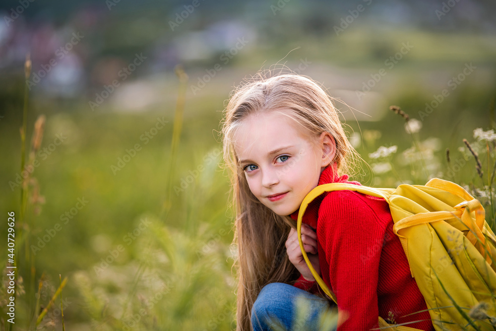 portrait of a child girl in a red jumper with a backpack traveling on a summer evening against backdrop of landscape. portrait of a child girl in a red jumper with a backpack traveling on a summer evening against backdrop of landscape.