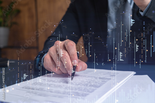 A client in formal wear is signing the contract to invest money in stock market. Internet trading and wealth management concept. Forex and financial hologram chart over the desk.