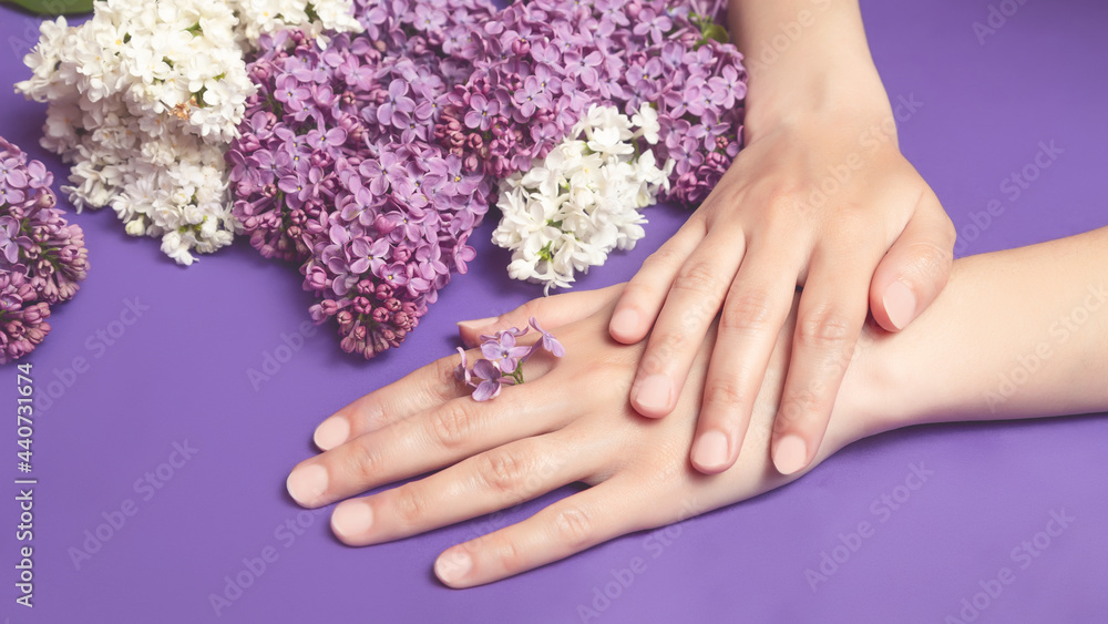 Fototapeta premium Close-up of beautiful sophisticated female hands with pink lilac flowers on a white background. Hand care concept, anti-wrinkle, anti-aging cream, spa