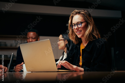 Smiling young businesswoman using laptop with team in the background