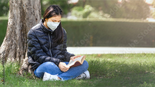 Asian Young girl intend to enjoy reading book for preparing final test exam sitting under trees at park outdoor on learn time in summer day. Education Learning Studying concept. Crop 16:9 Ratio. photo