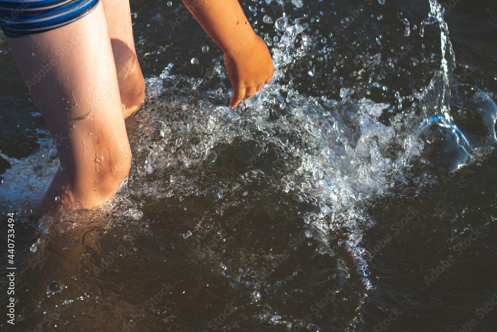 Young kid play in water and making splash boy to prepare in lake or river and have fun with drops.Closeup. Young kid play in water and making splash boy to prepare in lake or river and have fun with drops.Closeup.