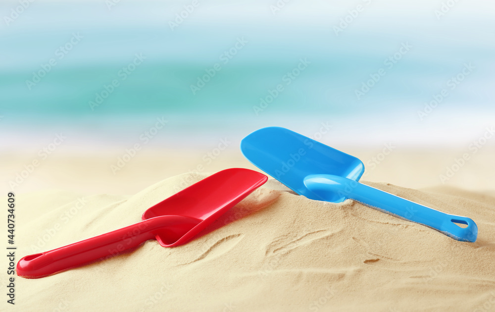 Red and blue plastic toy shovels on sandy beach near sea Red and blue plastic toy shovels on sandy beach near sea