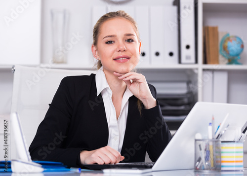 Smiling woman sitting at table and working on laptop in office © JackF