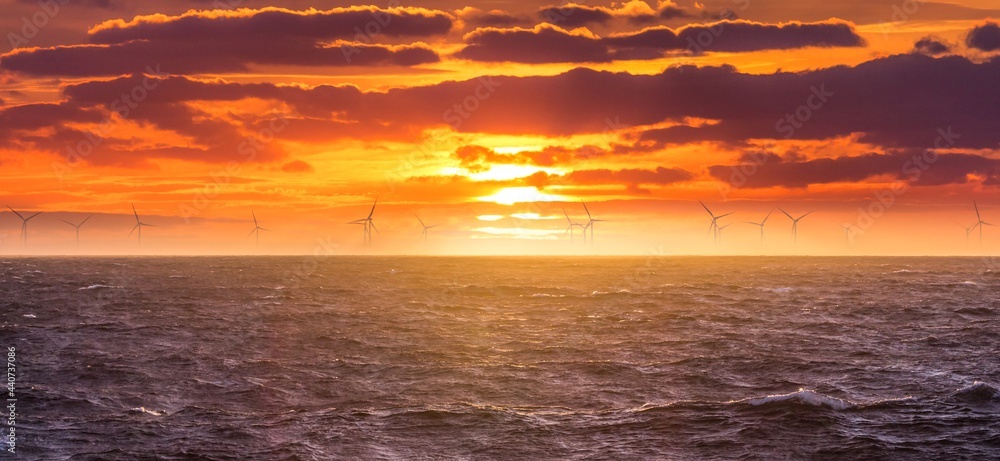 Renewable green electricity wind power generation offshore. Sunrise at decarbonization industry windmills business for regenerative energies. Clean energy renewables preventing climate change