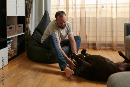 smiling middle-aged man petting his belly-up dog in his living room at sunset