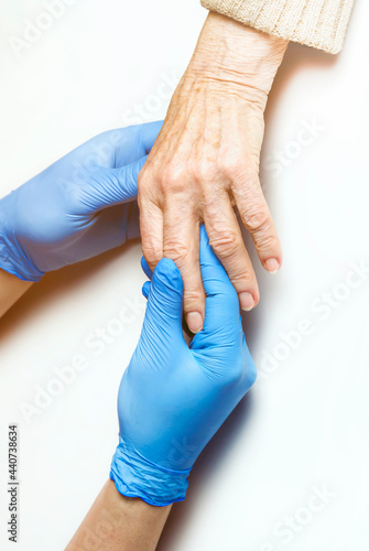 Doctor's hands in a blue gloves holds the hands of an elderly woman, a patient. Handshake, caring, trust and support. Medicine and healthcare.