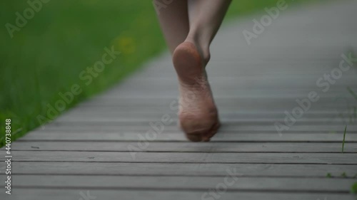 barefooted woman is walking on wood path in park at summer day, closeup of feet