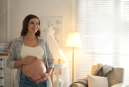Fotografie Happy pregnant woman touching her belly indoors