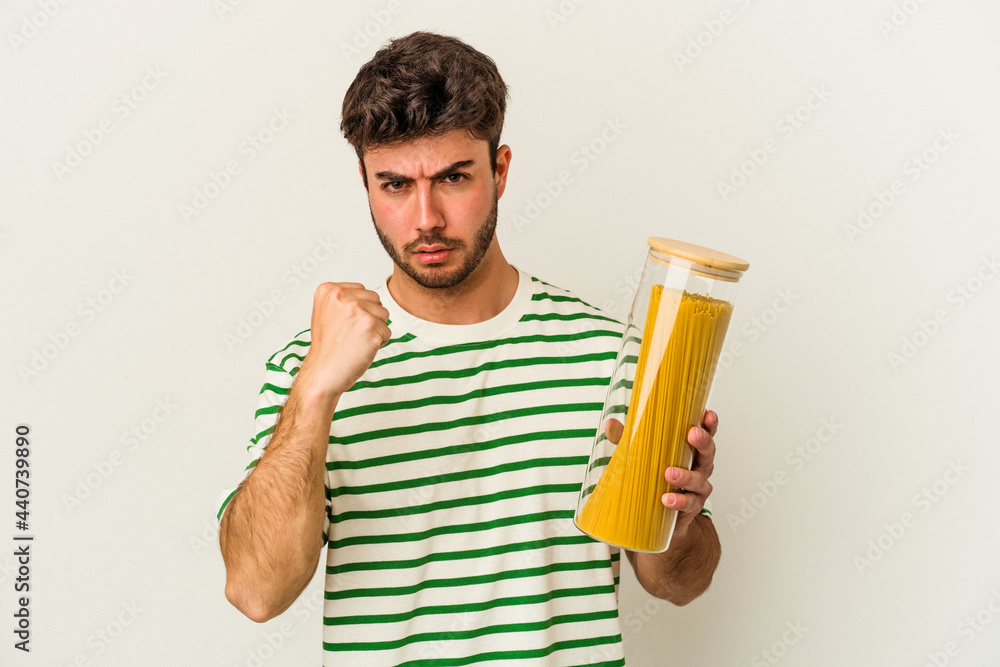Young caucasian woman holding pasta jar isolated on white background showing fist to camera, aggressive facial expression. Young caucasian woman holding pasta jar isolated on white background showing fist to camera, aggressive facial expression.