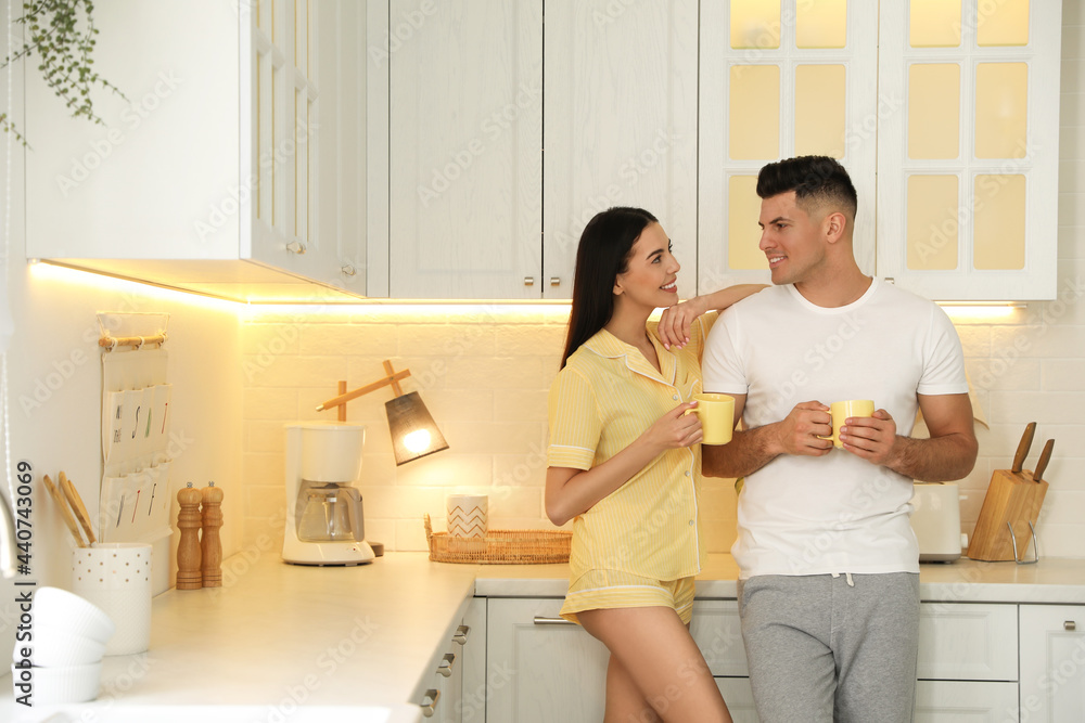 Happy couple wearing pyjamas with cups of coffee in kitchen Happy couple wearing pyjamas with cups of coffee in kitchen
