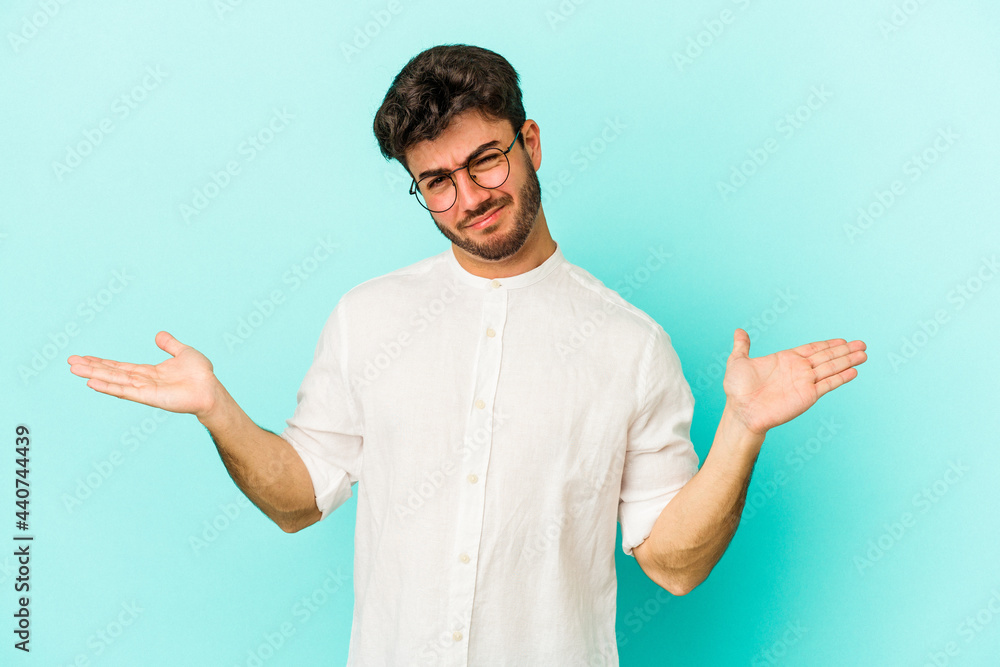 Young caucasian man isolated on blue background doubting and shrugging shoulders in questioning gesture. Young caucasian man isolated on blue background doubting and shrugging shoulders in questioning gesture.