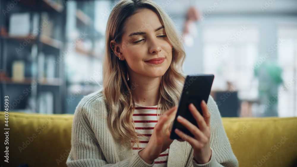 Beautiful Caucasian Female Using Smartphone in Stylish Living Room while Resting on a Cozy Couch Sofa. Young Woman at Home, Browsing Internet, Using Social Networks, Having Fun in Flat. Beautiful Caucasian Female Using Smartphone in Stylish Living Room while Resting on a Cozy Couch Sofa. Young Woman at Home, Browsing Internet, Using Social Networks, Having Fun in Flat.