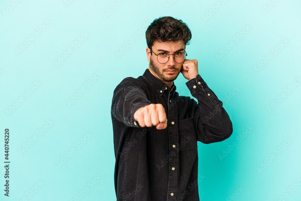 Young caucasian man isolated on blue background throwing a punch, anger, fighting due to an argument, boxing. Young caucasian man isolated on blue background throwing a punch, anger, fighting due to an argument, boxing.