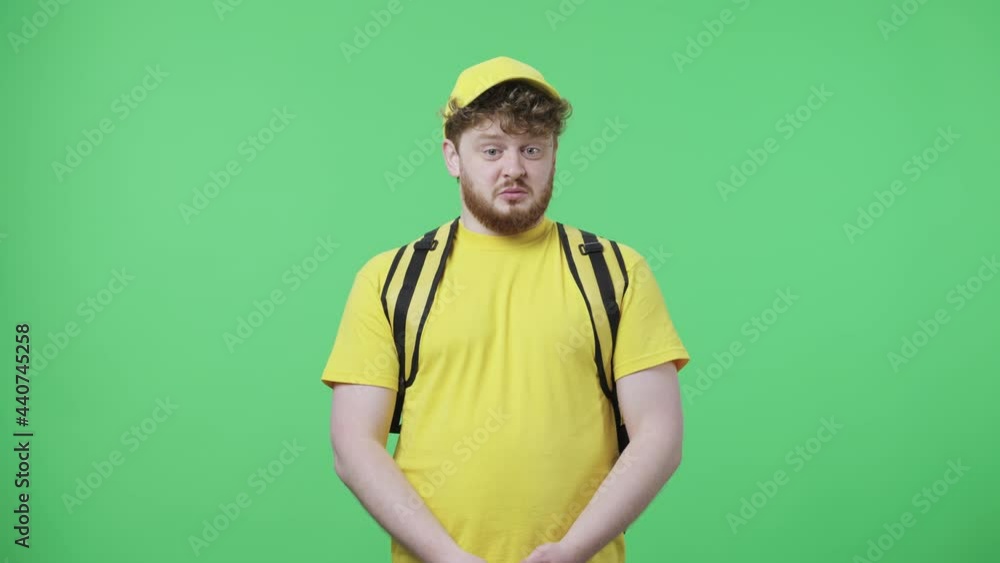 Portrait of young men looking at camera with dislike and disgust. Redhead male in yellow delivery courier uniform with thermo bag posing on green screen in studio. Close up. Slow motion ready 59.97fps Portrait of young men looking at camera with dislike and disgust. Redhead male in yellow delivery courier uniform with thermo bag posing on green screen in studio. Close up. Slow motion ready 59.97fps