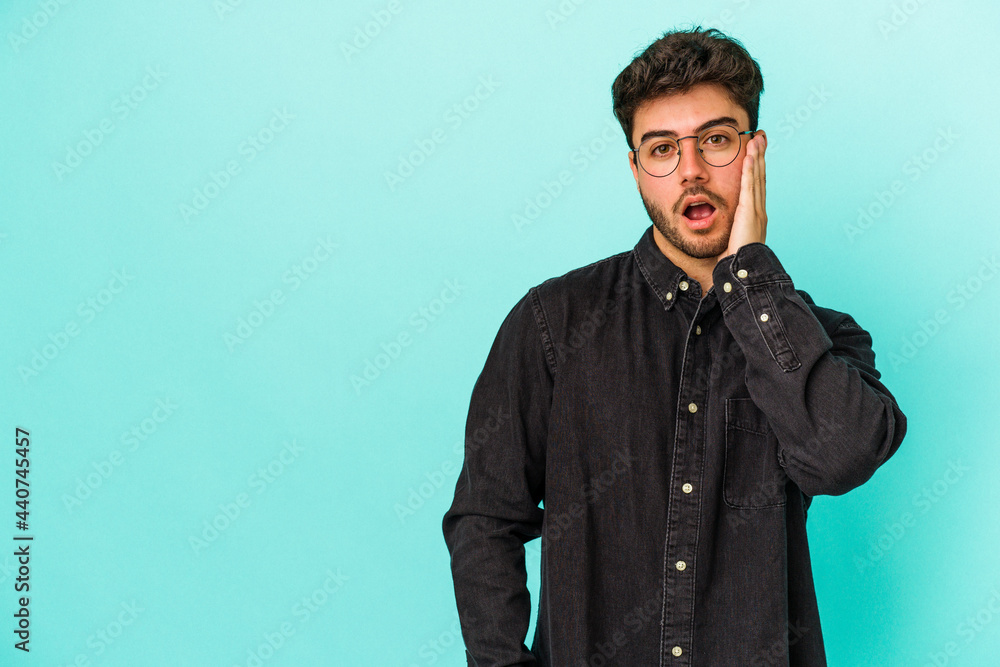 Obraz premium Young caucasian man isolated on blue background shouts loud, keeps eyes opened and hands tense.