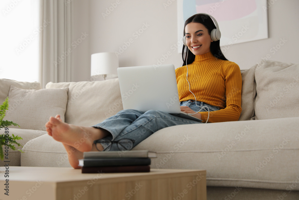 Woman with laptop and headphones sitting on sofa at home Woman with laptop and headphones sitting on sofa at home