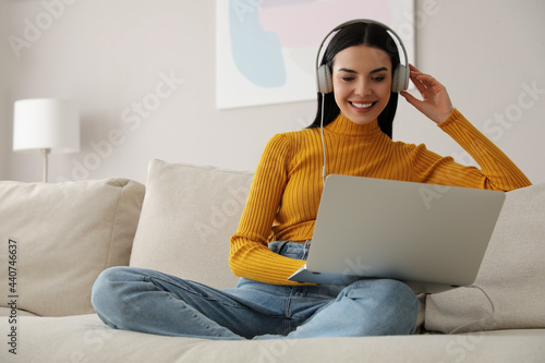 Woman with laptop and headphones sitting on sofa at home photo