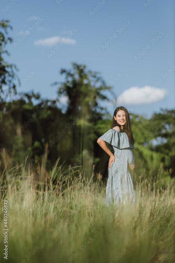 Asian young pregnant woman in blue dress relaxing and enjoying life in grass nature at summer day. Healthy pregnant. Copy space Asian young pregnant woman in blue dress relaxing and enjoying life in grass nature at summer day. Healthy pregnant. Copy space