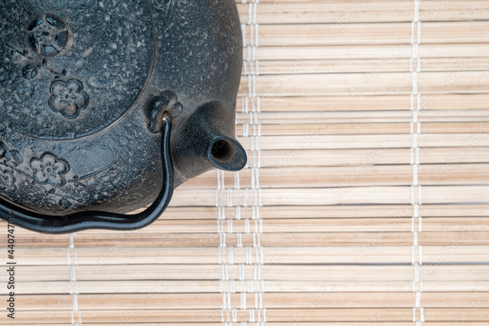 Obraz premium Vintage, black metal Japanese tea pot on a reed pad with a lot of free space. Minimalistic tea ceremony concept.