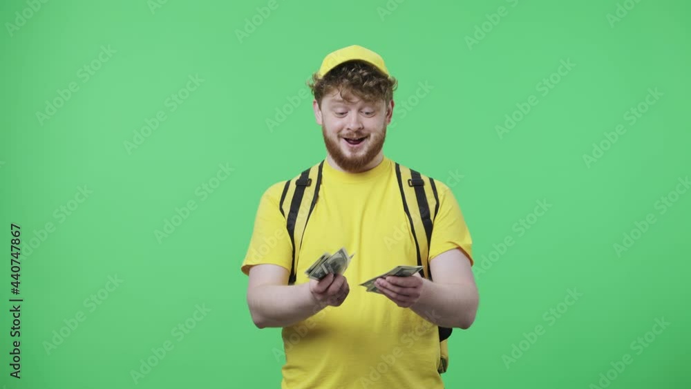 Portrait of young men counting money and is very happy with salary or tip. Redhead male in yellow delivery courier uniform with thermo bag posing on green screen. Close up. Slow motion ready 59.97fps. Portrait of young men counting money and is very happy with salary or tip. Redhead male in yellow delivery courier uniform with thermo bag posing on green screen. Close up. Slow motion ready 59.97fps.