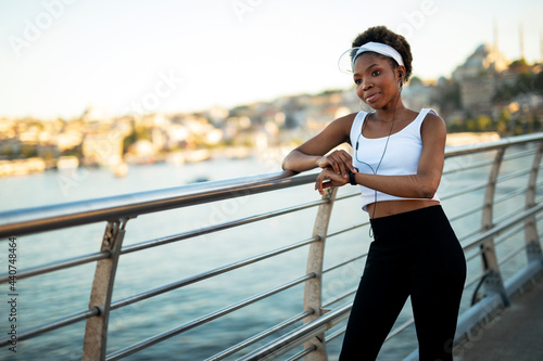 Young african woman training outdoors. Female runner using smart watch...