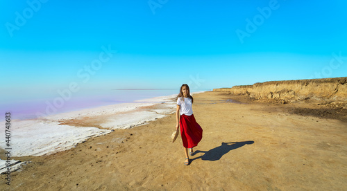 Woman wearing red skirt walking at sandy beach with blue sky near salt pink lake