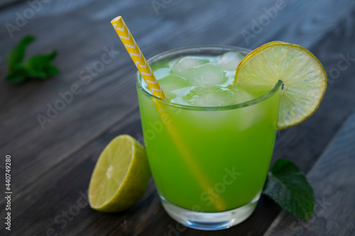 green drink or cocktail in a glass with a slice of lime and mint on a dark wooden background