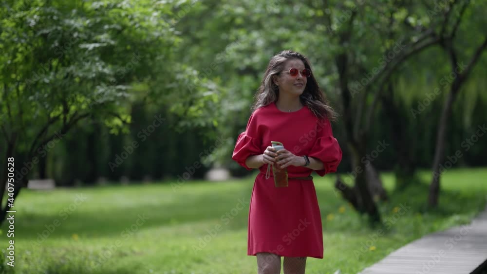 positive woman is strolling alone in park at summer day, smiling and admiring nature positive woman is strolling alone in park at summer day, smiling and admiring nature