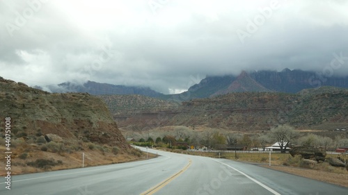 Road trip, driving auto in Zion Canyon, Utah, USA. Hitchhiking traveling in America, autumn journey. Red alien steep cliffs, rain and bare trees. Foggy weather and calm fall atmosphere. View from car. © Dogora Sun