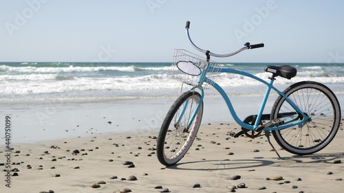 Blue bicycle, cruiser bike by ocean beach pacific coast, Oceanside California USA. Summertime vacations, sea shore. Vintage cycle on sand. Clear sky and water waves. Waterfront summer near Los Angeles