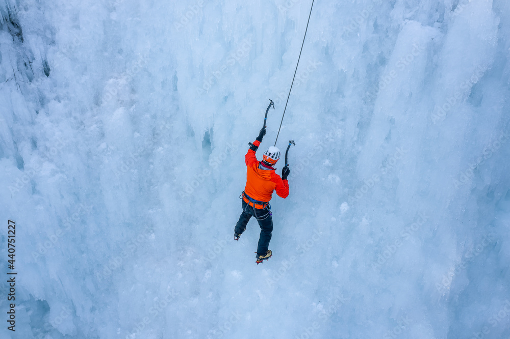 Aerial shot of a Caucasian man climbing frozen waterfall, using front pointing technique, close to the top